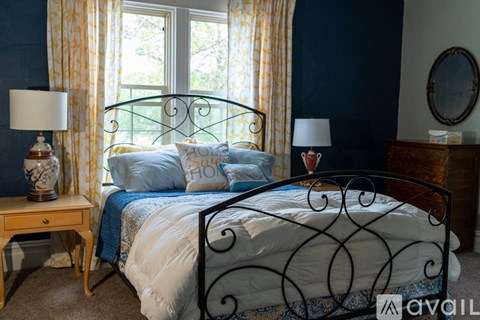 A bedroom with a black metal bed frame and a window with yellow curtains.