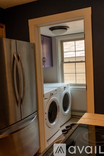 A stainless steel refrigerator is next to a washing machine in a kitchen.