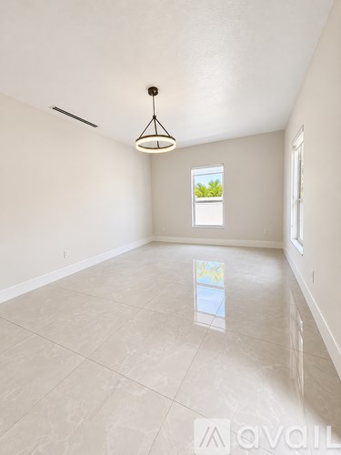 A large empty room with a window and a hanging light fixture.