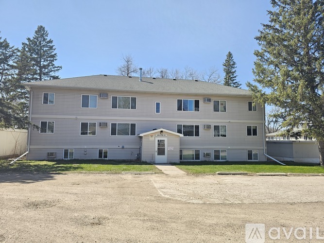A large, two-story building with a garage door is surrounded by trees and has a clear blue sky above.