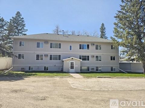 A large, two-story building with a garage door is surrounded by trees and has a clear blue sky above.