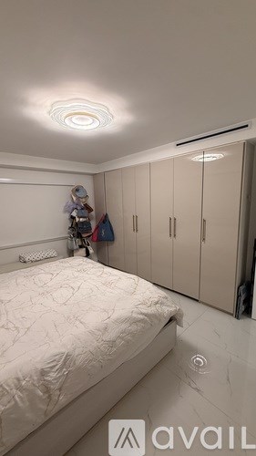 A bedroom with a bed, a ceiling light, and a person standing by the wardrobe.