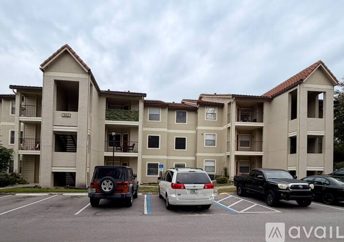 A parking lot in front of a beige apartment building with several cars parked.