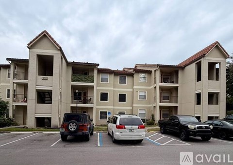 A parking lot in front of a beige apartment building with several cars parked.