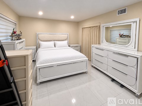 A white bedroom with a bed, dresser, and mirror.
