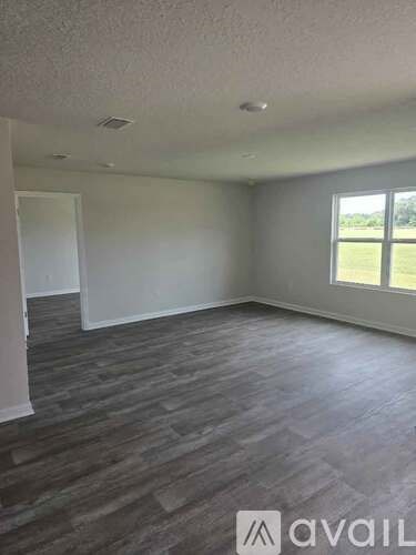 A room with grey flooring and a window overlooking a green field.