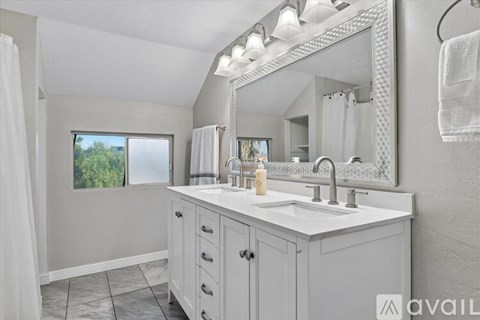 A bathroom with a large mirror, a white sink, and a window with a view of trees.