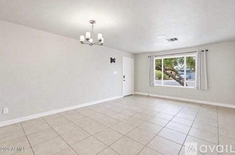 A spacious room with a chandelier, tiled floor, and a window with a view of the outdoors.