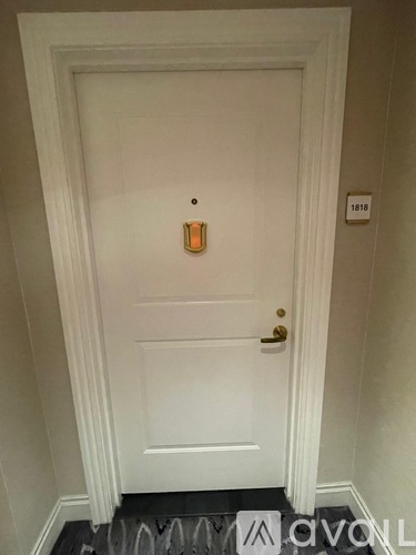 A white door with a gold handle and a number plate on the wall.