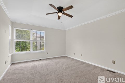 A spacious room with a ceiling fan and a window overlooking a fence.