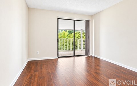A room with wooden floors and a sliding glass door leading to a balcony.