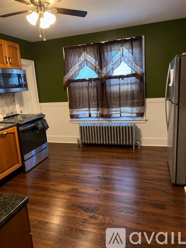 A kitchen with a refrigerator, stove, and window with curtains.