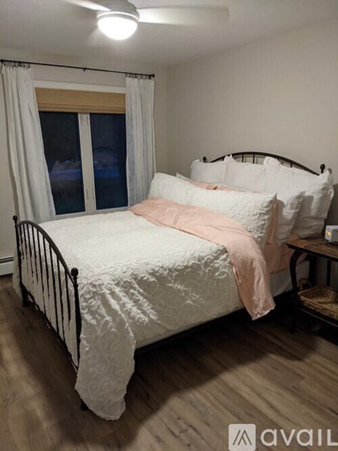 A bedroom with a bed, a window with curtains, and a nightstand with a lamp.