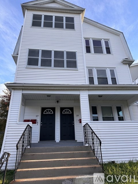 A white two-story house with a black front door and stairs leading up to it.