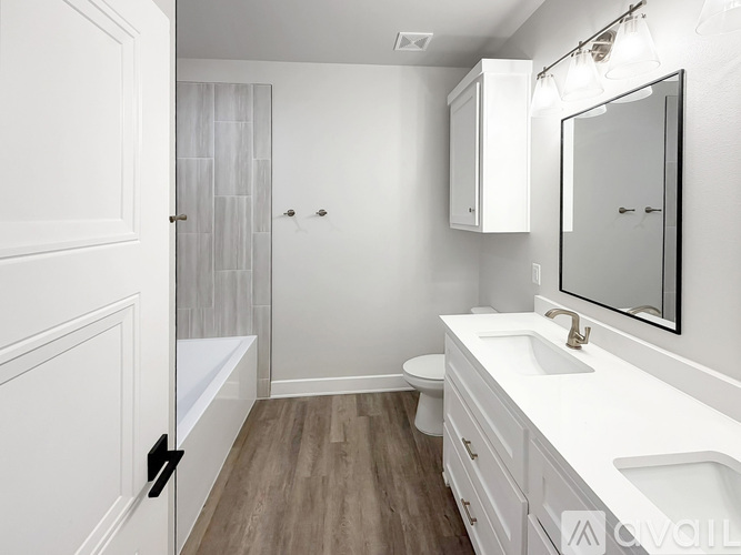 A white bathroom with wood flooring and a white toilet.