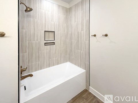 A white bathtub in a bathroom with a grey tiled wall.