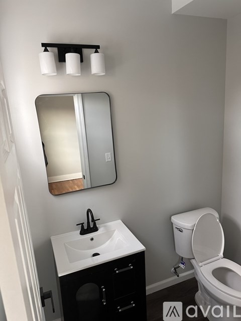 A bathroom with a toilet, sink, mirror and lights.