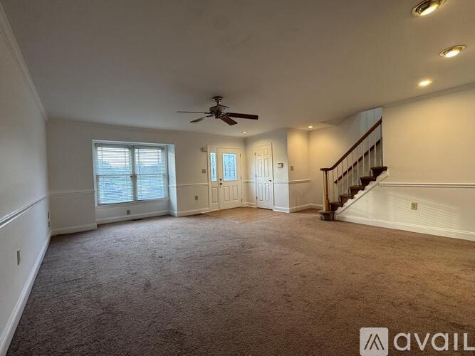 A spacious room with a carpeted floor, a ceiling fan, and a staircase.