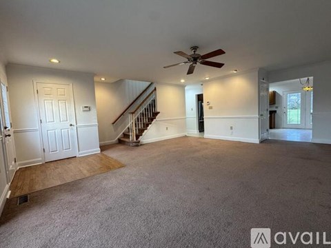 A spacious living room with a staircase and a ceiling fan.