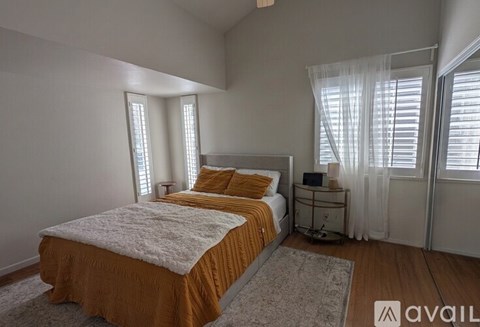 A bedroom with a bed, nightstand, and window with curtains.