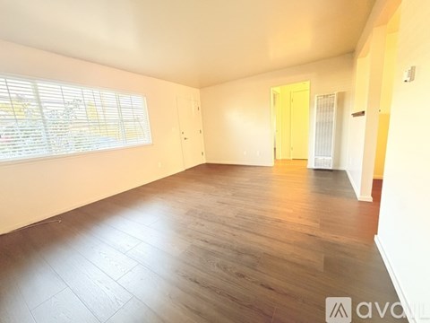 A spacious room with wooden flooring and a window with blinds.