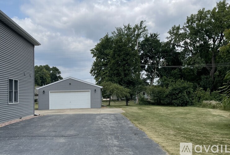 A large grey garage with a white door is situated in a grassy area with trees in the background.