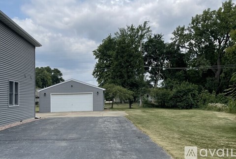 A large grey garage with a white door is situated in a grassy area with trees in the background.
