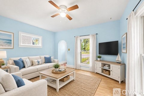 A living room with a white sofa, a coffee table, a television, and a window with white curtains.