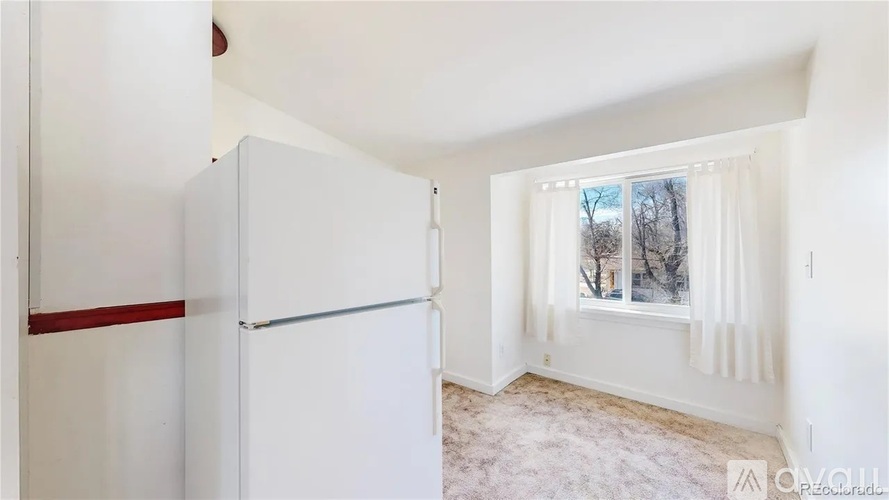 A white refrigerator in a room with a window showing trees outside.