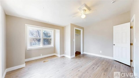 A spacious room with a window, a door, and a ceiling fan.