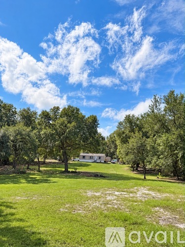 A grassy field with trees and a house in the distance.