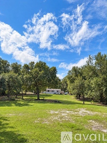 A grassy field with trees and a house in the distance.
