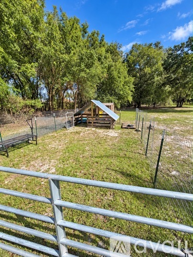 A small wooden structure sits in a grassy field behind a chain link fence.