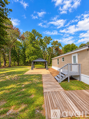 A wooden deck leads to a small house with a porch and a gazebo in the yard.