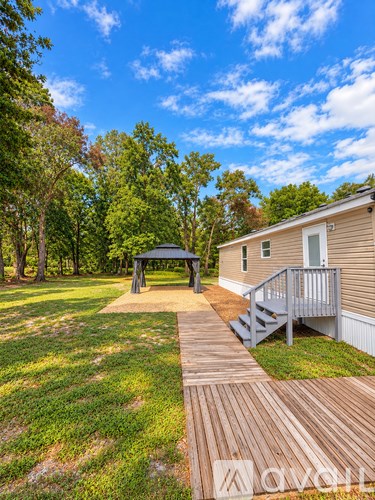 A wooden deck leads to a small house with a porch and a gazebo in the yard.