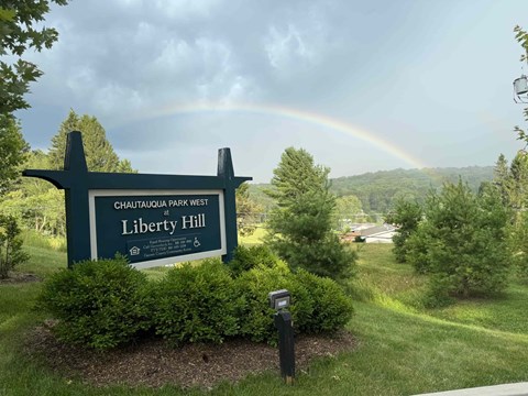 A sign for Chautauqua Park West Liberty Hill with a rainbow in the background.