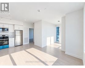A spacious, empty living room with a kitchen area in the background.