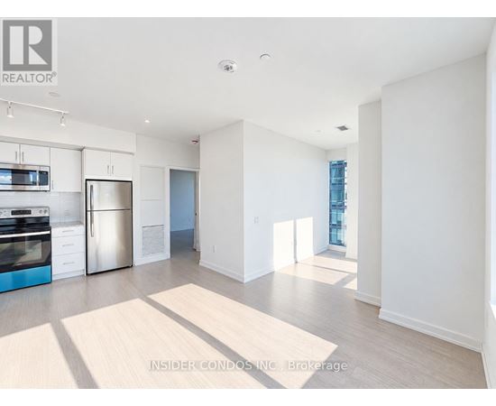 A spacious, empty living room with a kitchen area in the background.