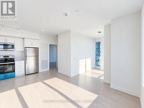 A spacious, empty living room with a kitchen area in the background.