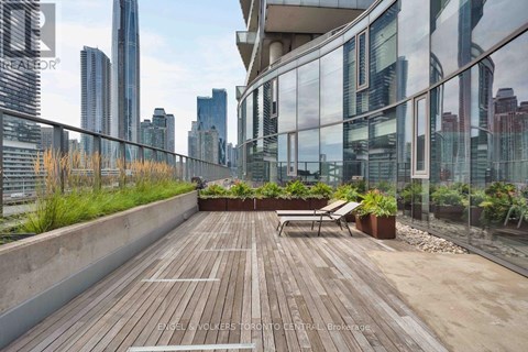 A wooden deck with a bench and potted plants on a balcony overlooking a city skyline.