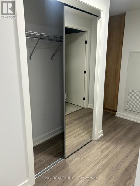 A hallway with a mirrored closet door and wooden floors.