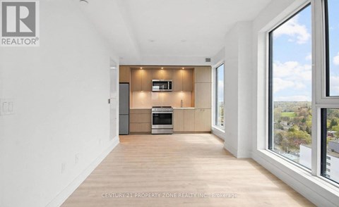 A spacious, well-lit room with a kitchen area and a large window overlooking a landscape.