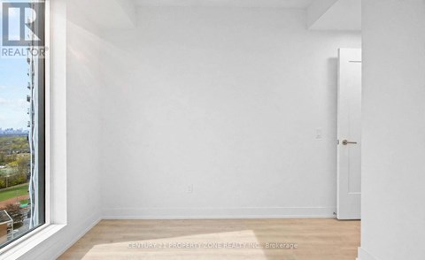 A white room with a door and a window overlooking a tree-filled landscape.