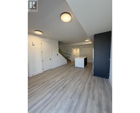 A room with a wooden floor and a staircase in the background.