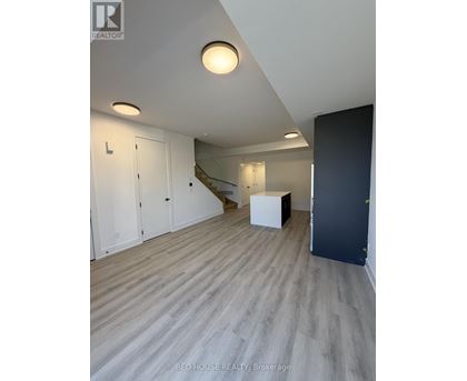 A room with a wooden floor and a staircase in the background.