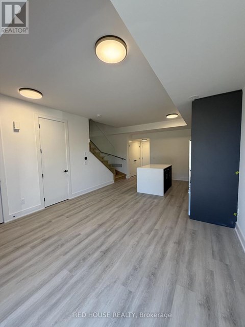A room with a wooden floor and a staircase in the background.