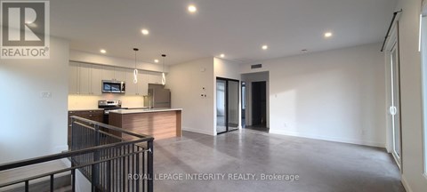 A spacious, empty living room with a kitchen area in the background.