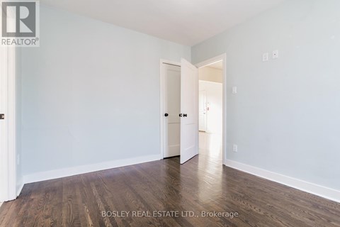 A room with a wooden floor and white walls, with a door on the left and an open doorway on the right.