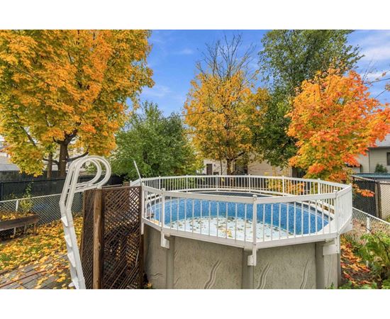 A small above ground pool surrounded by a fence and trees with autumn leaves.