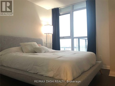 A bedroom with a large bed and a window with curtains.